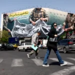 Warga Teheran melewati poster menentang AS/ Foto: the guardian