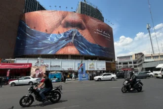 Papan reklame dengan gambar Selat Hormuz dan bibir Presiden AS Donald Trump yang dijahit di sebuah alun-alun di pusat kota Teheran /Foto: AP News