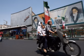Orang-orang berkendara melewati mural yang menggambarkan mendiang pemimpin tertinggi, Ayatollah Ruhollah Khomeini, di Teheran/ Foto: The Guardian