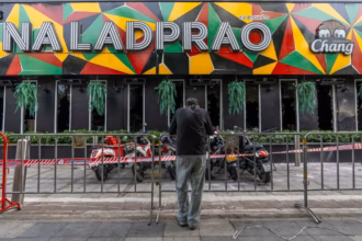 Seorang pelayat berdiri di luar pub di Bangkok tempat puluhan orang tewas dalam kebakaran pada hari Senin/ Foto: The Guardian.