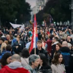 Seorang pria memegang bendera Serbia saat orang-orang berkumpul rapat umum terakhir Daftar Mahasiswa di Belgrade, Serbia, pada 22 Oktober 2026, menjelang pemilihan parlemen / Foto: AP