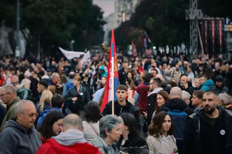 Seorang pria memegang bendera Serbia saat orang-orang berkumpul rapat umum terakhir Daftar Mahasiswa di Belgrade, Serbia, pada 22 Oktober 2026, menjelang pemilihan parlemen / Foto: AP